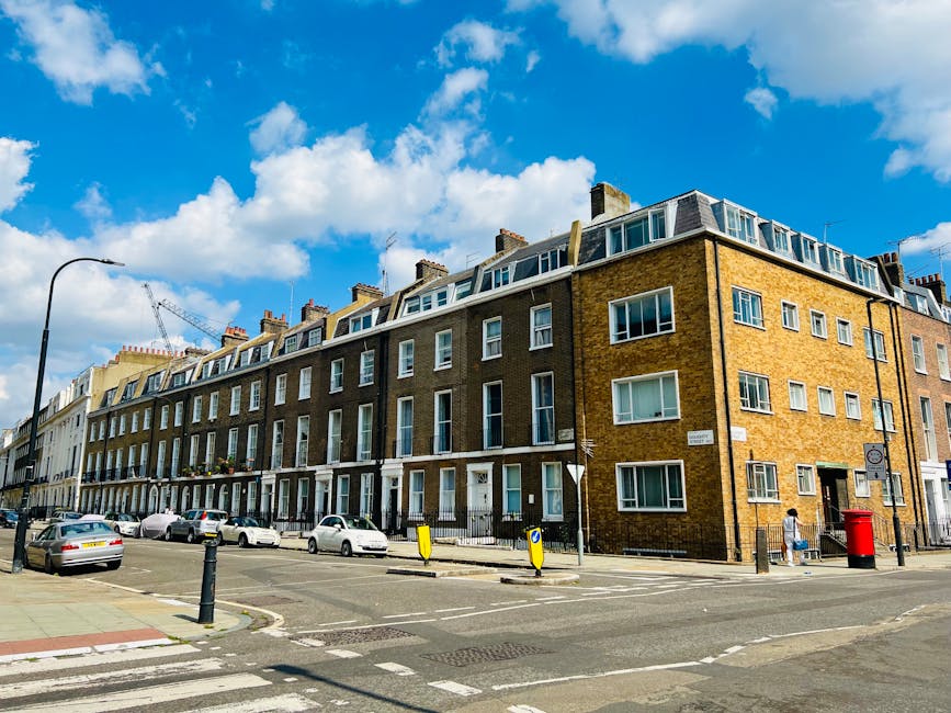An empty residential street in Islington with Victorian-style terraced houses featuring white and brick facades, terracotta roof tiles, and decorative bay windows. The street has a paved sidewalk on the right with a black wrought-iron fence and a few small plants, and a tarmac road on the left with clear road markings. Overhead, the sky is cloudy, casting diffused natural light, highlighting the clean, well-maintained surfaces of the buildings and pavement. The scene reflects a quiet, tidy neighborhood with a focus on urban cleanliness, representative of the type of environment that Cleaner Islington services for end of tenancy and domestic cleaning, ensuring hygienic, polished finishes for both residential exteriors and interiors.
