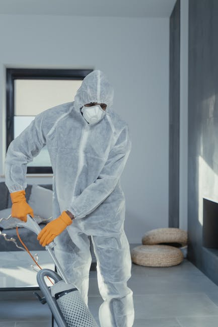 A handheld vacuum cleaner with a silver telescopic tube and black attachments resting on a light wooden floor near a white wall with baseboards. The vacuum is positioned diagonally, with the cleaning 